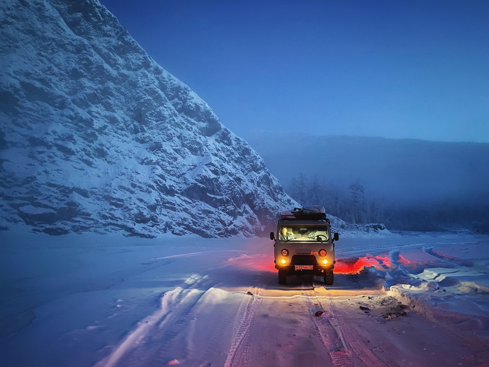 汽车停在冰雪覆盖的道路上，旁边是皑皑雪山。